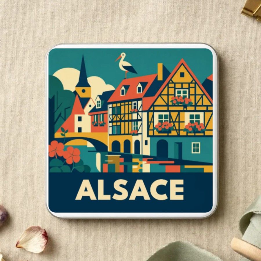 Magnet souvenir d’Alsace en style géométrique années 50 : les maisons à colombages fleuries au bord du canal, un clocher et une cigogne, nom en grandes capitales